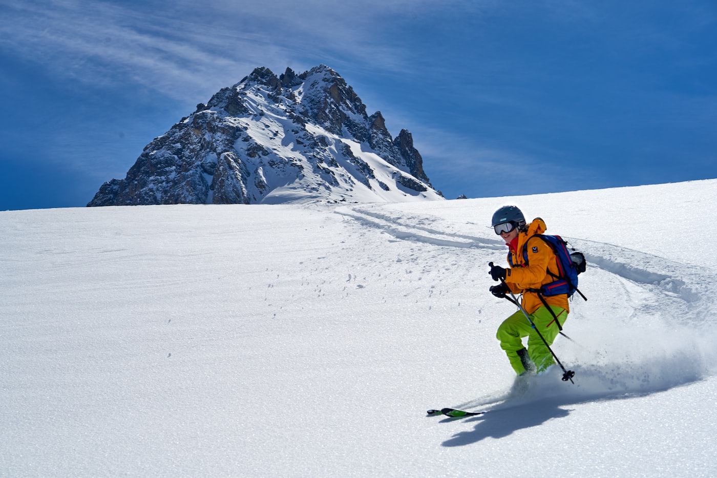 A skier in an orange jacket descending an open snow face